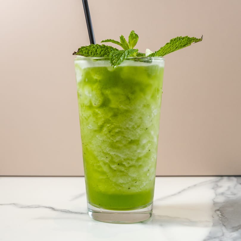 Refreshing green smoothie with mint leaves and a black straw, on a marble surface.