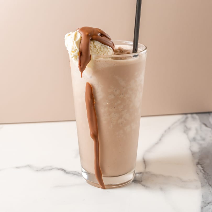 Chocolate milkshake in a tall glass with a scoop of vanilla ice cream and chocolate syrup.