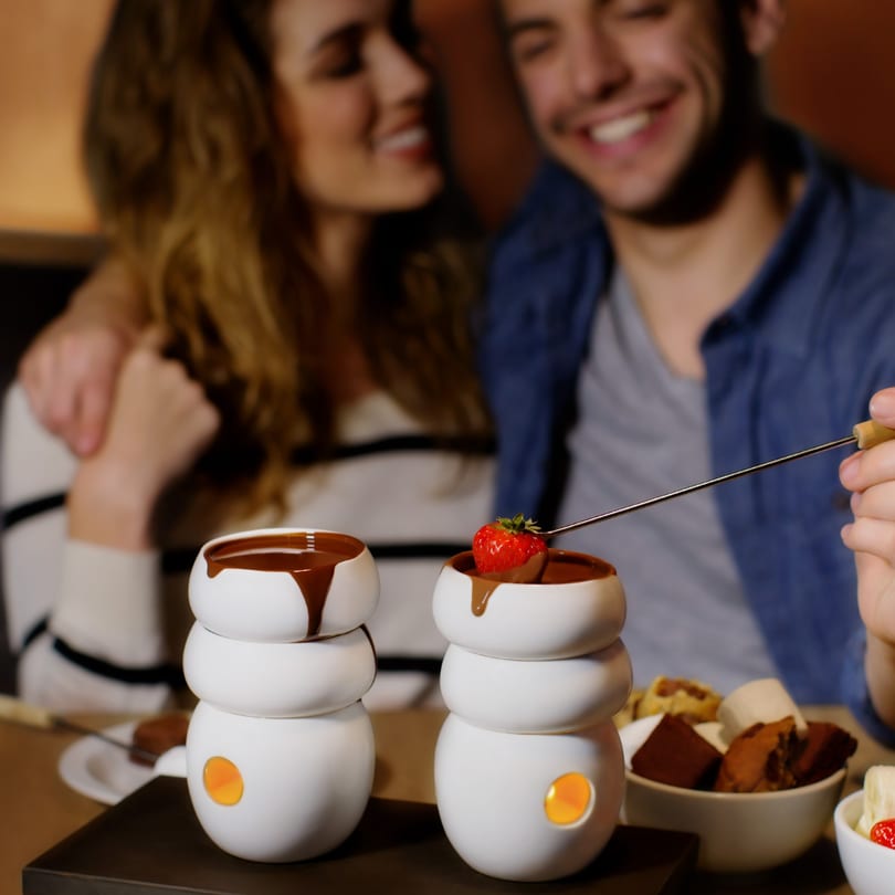 A couple enjoying chocolate fondue at Max Brenner, dipping a strawberry into melted chocolate.
