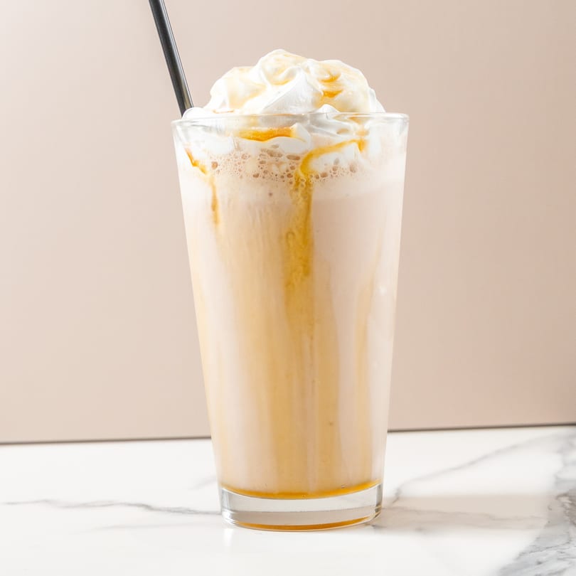 Caramel frappe with whipped cream and a black straw on a marble surface.