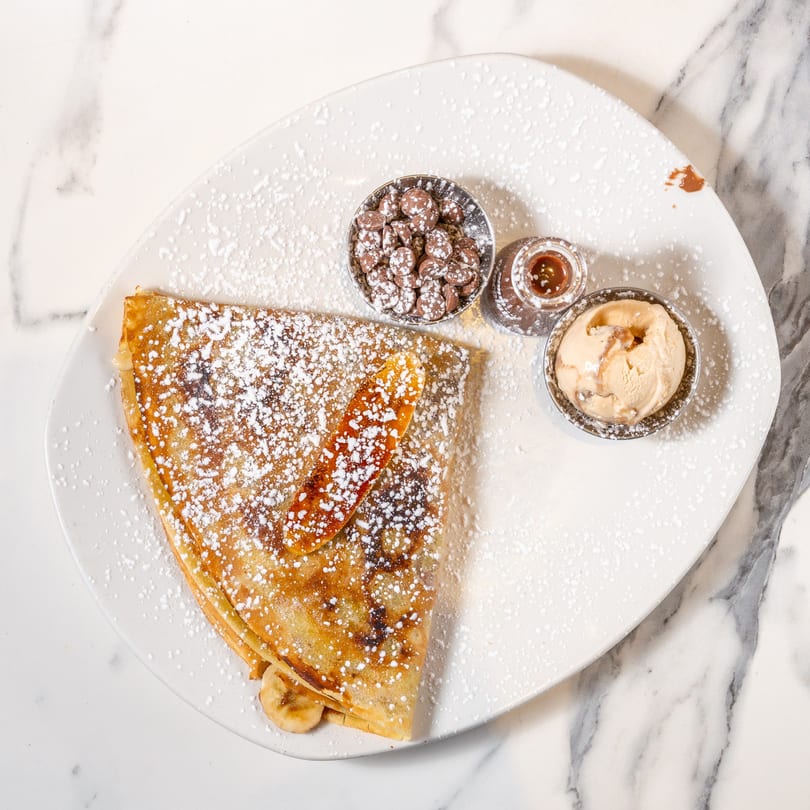 Banana crepe dusted with powdered sugar, served with chocolate chips, caramel, and ice cream.